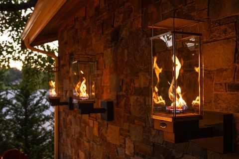 Black wood stove with a glowing fire burning inside against a stone wall.