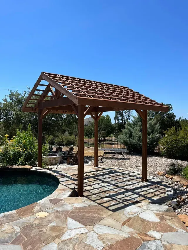 A wooden pergola is sitting next to a swimming pool.