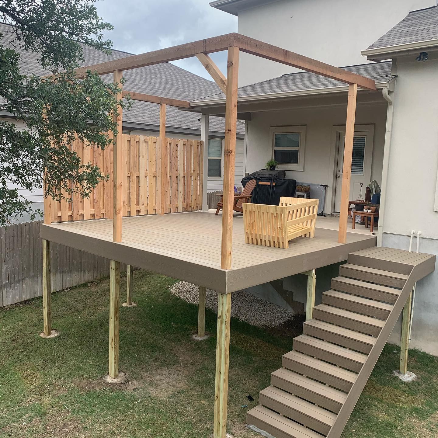 A wooden deck with stairs leading up to it is in the backyard of a house.