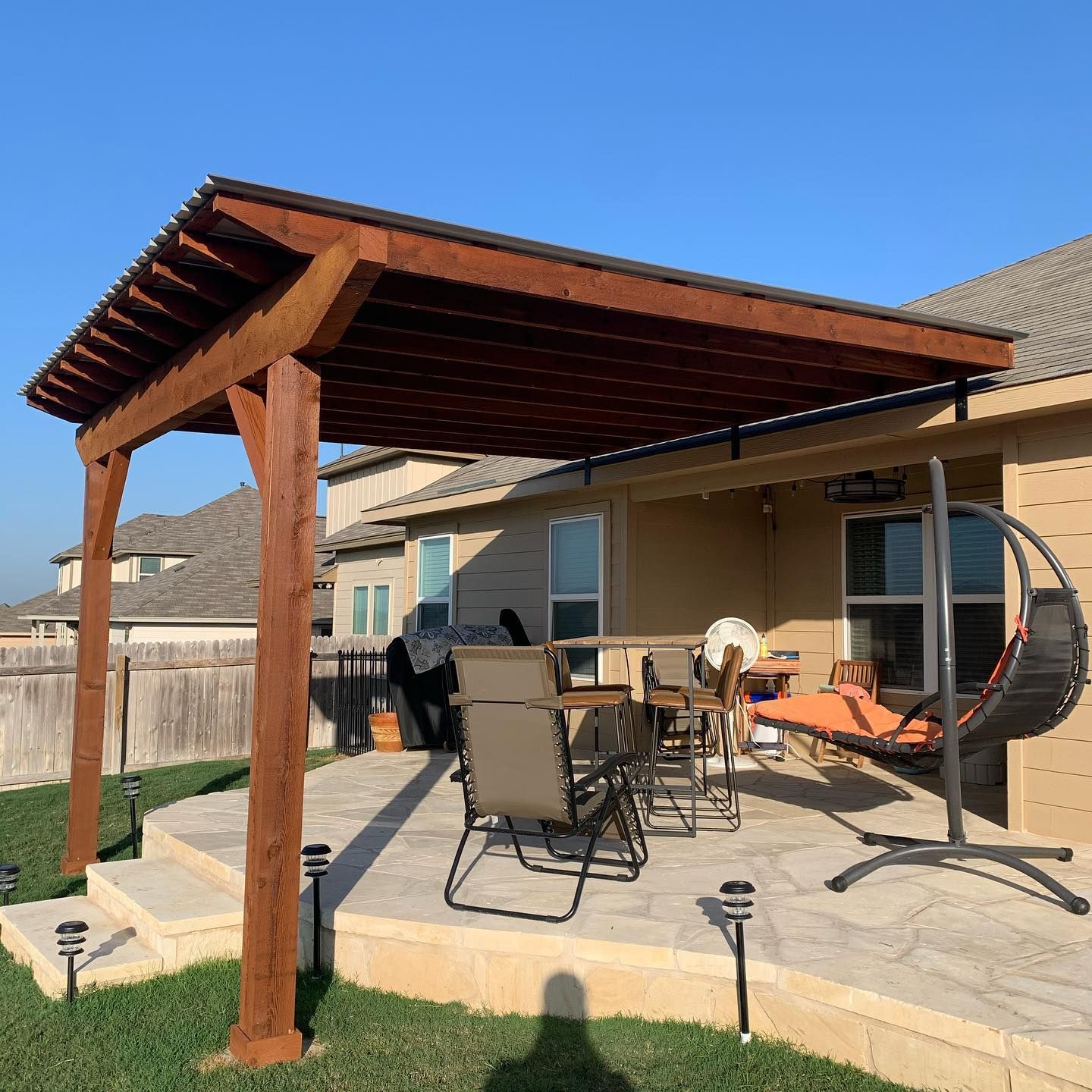 A wooden pergola is sitting on top of a patio with chairs and a swing.
