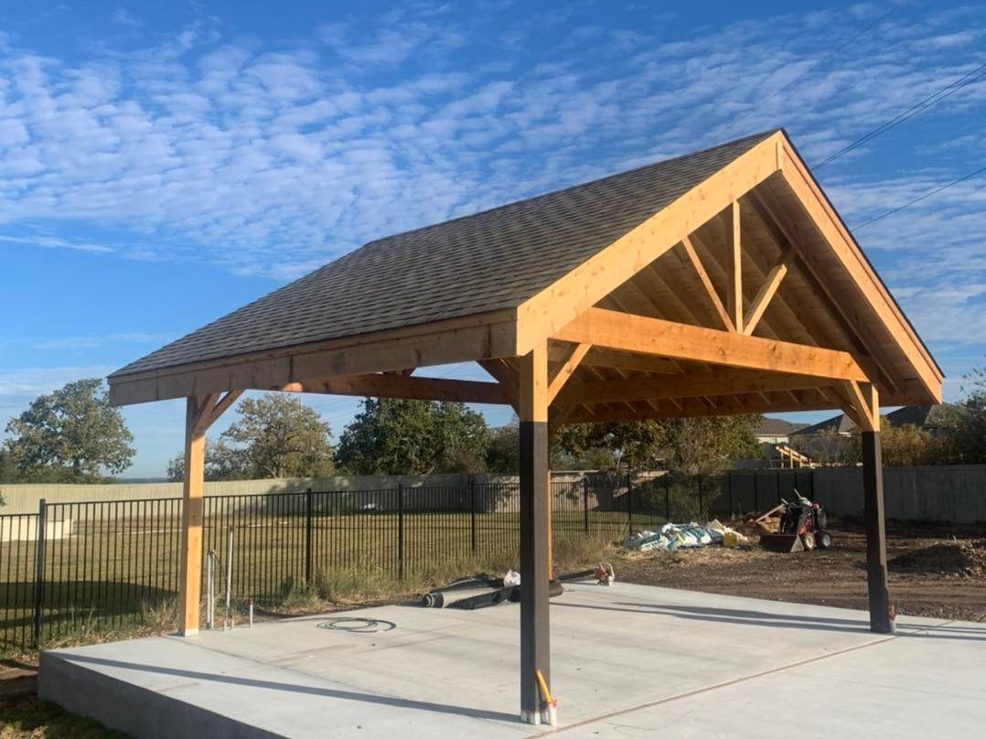 A wooden pavilion with a roof is being built in a backyard.