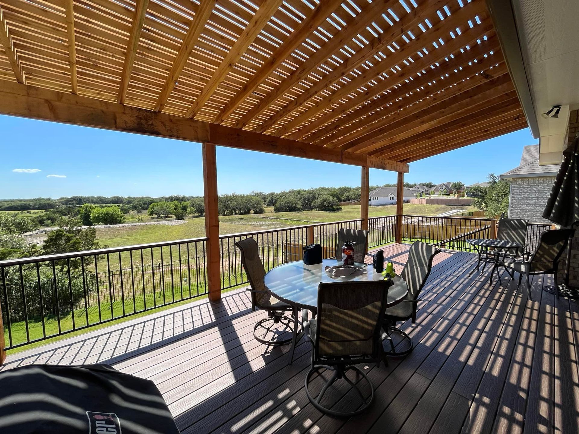 A wooden deck with a table and chairs under a pergola.