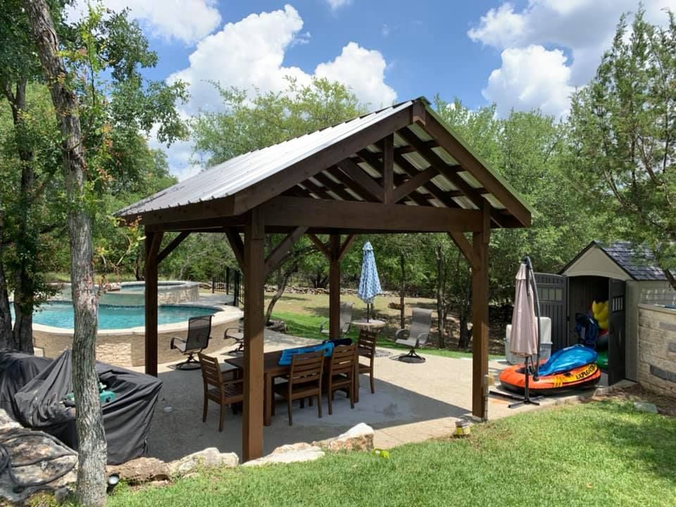 A wooden pavilion with a metal roof is in the backyard next to a pool.