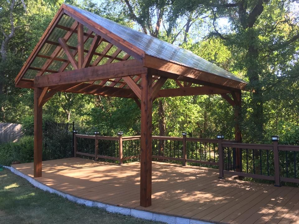 A wooden gazebo with a clear roof is surrounded by trees and a wooden deck.
