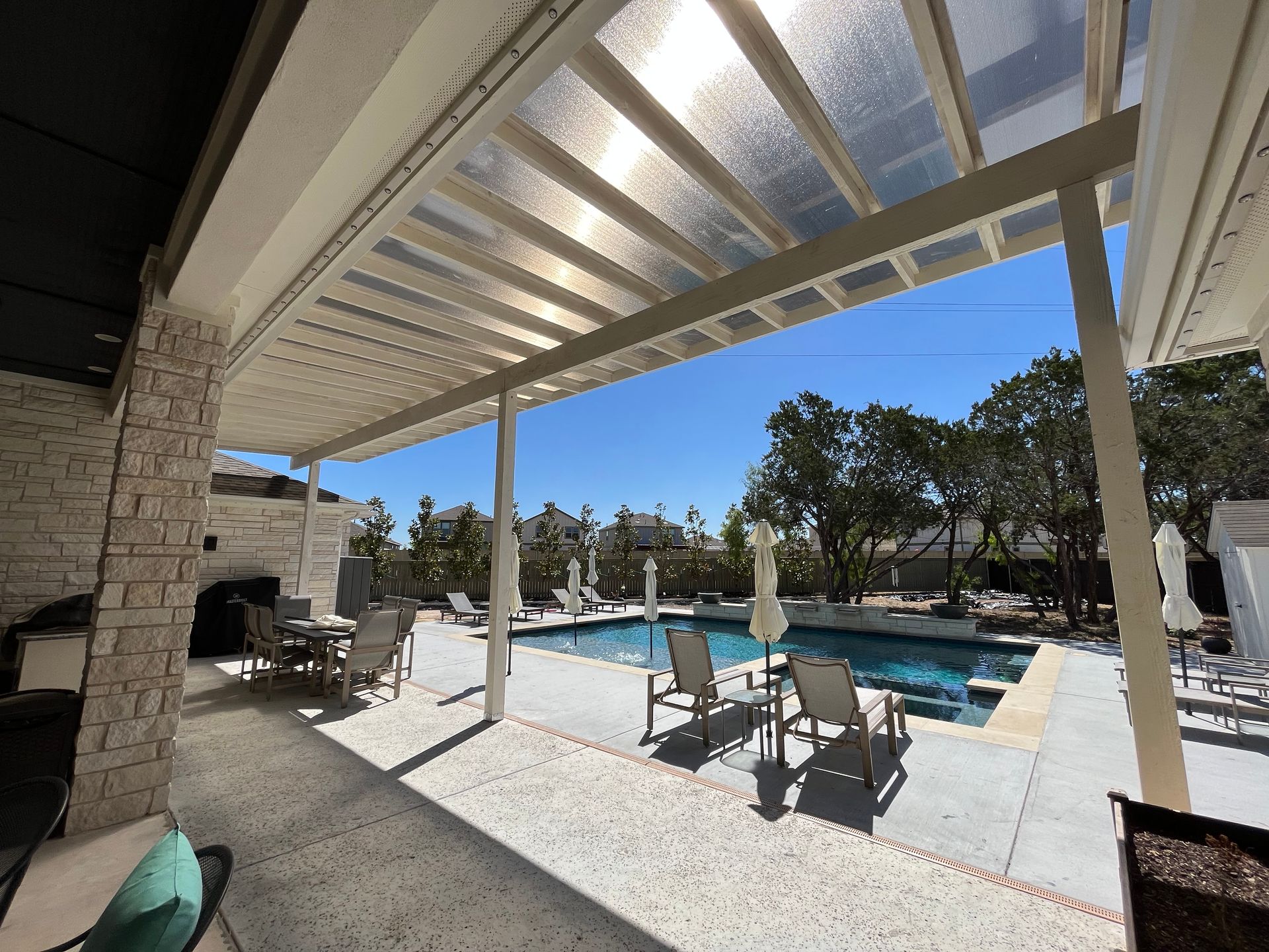 A patio with a swimming pool and chairs under a canopy.