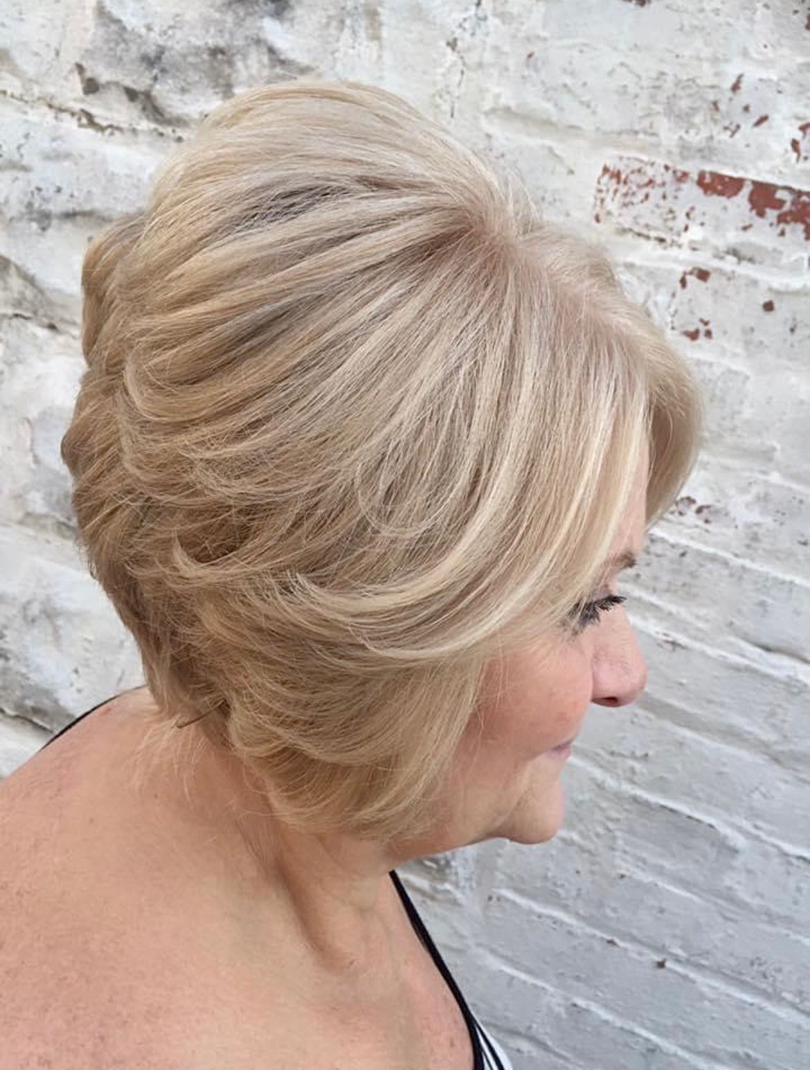 a woman with short blonde hair is standing in front of a white brick wall