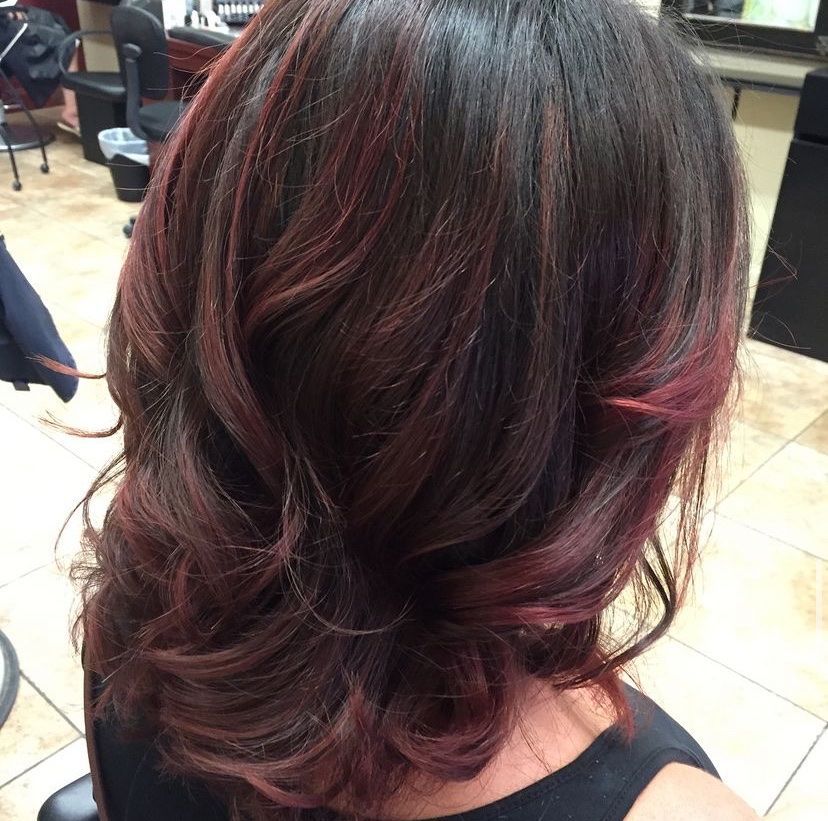 a woman with dark hair and red highlights is sitting in a chair