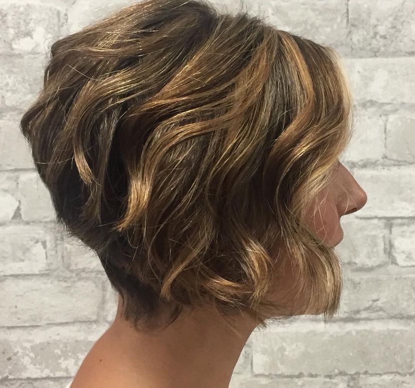 a woman with short wavy hair is standing in front of a white brick wall