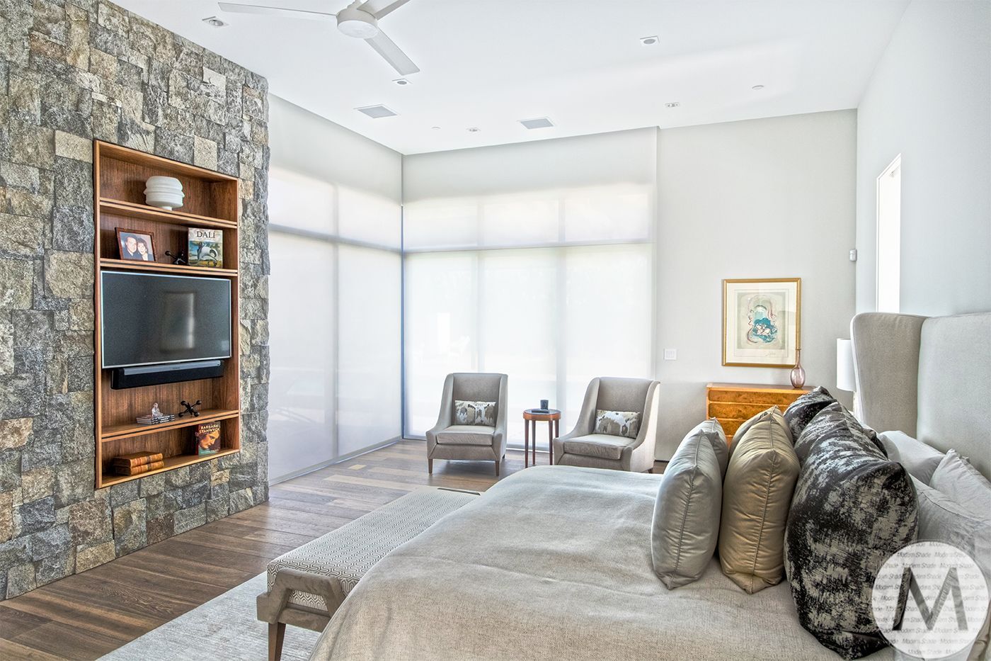 Spacious bedroom with stone wall, built-in TV, seating area, and king-size bed with decorative pillows.