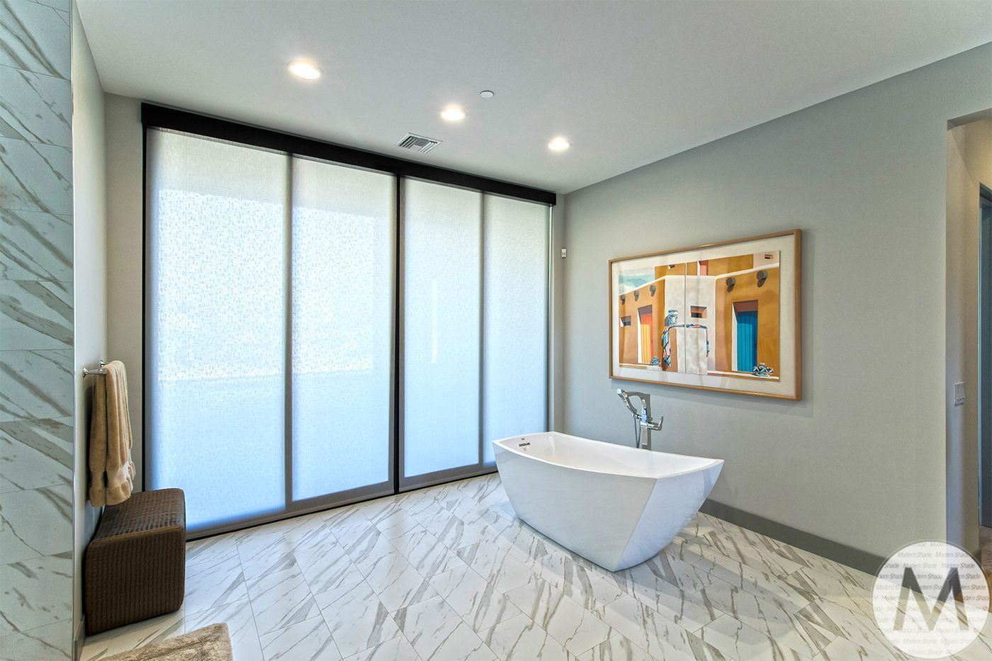 Modern bathroom with freestanding tub, art, and floor-to-ceiling frosted blinds. Gray walls, marble floor.