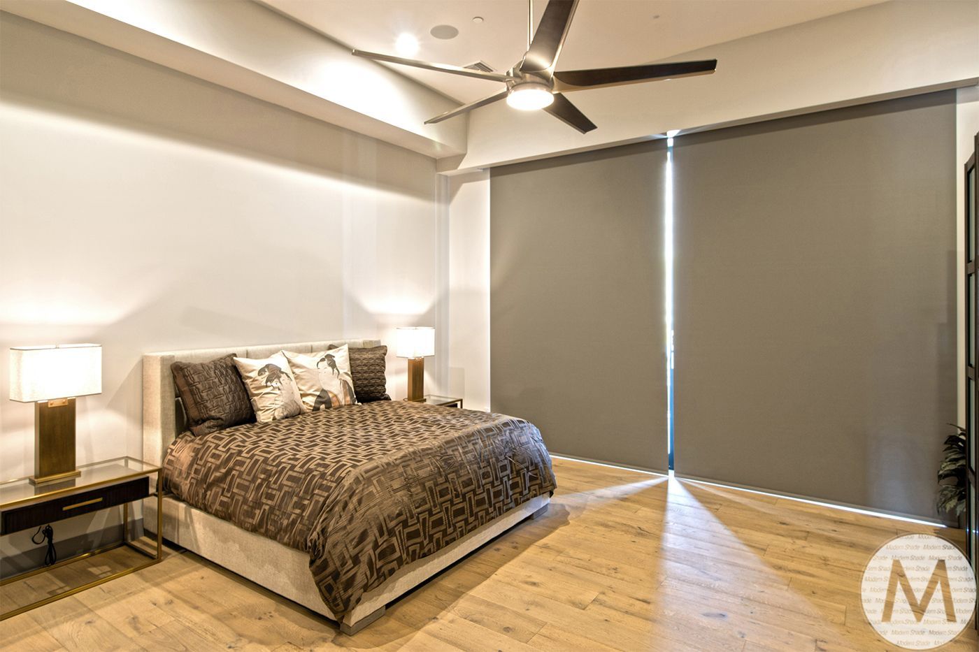 Bedroom with a bed, bedside tables with lamps, large window with grey shades, and a ceiling fan.