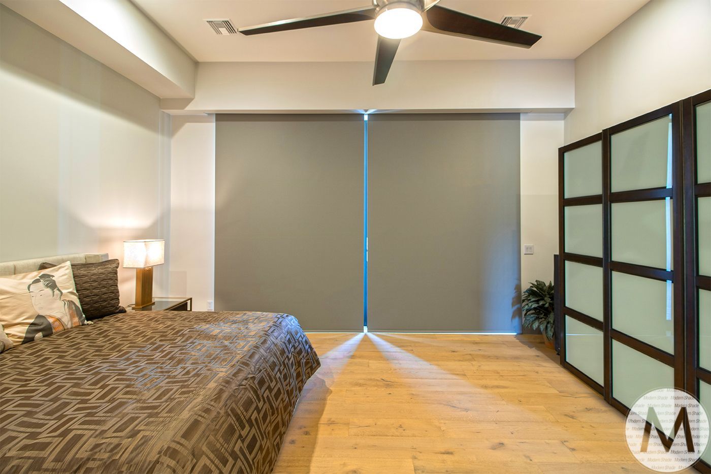 Bedroom with grey blinds, light wood floor, and dark wood closet.