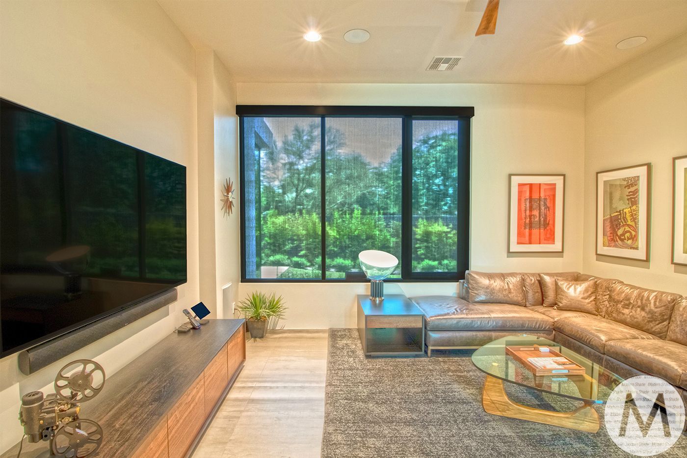Living room with a large TV, leather sectional, window with a view, and artwork.