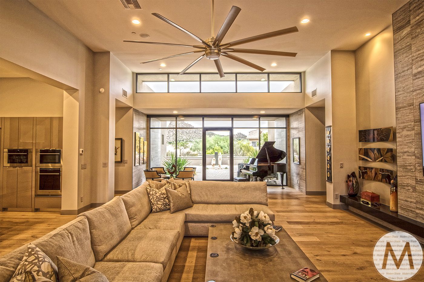 Spacious living room with a sectional sofa, grand piano, large fan, and open to outdoor patio.