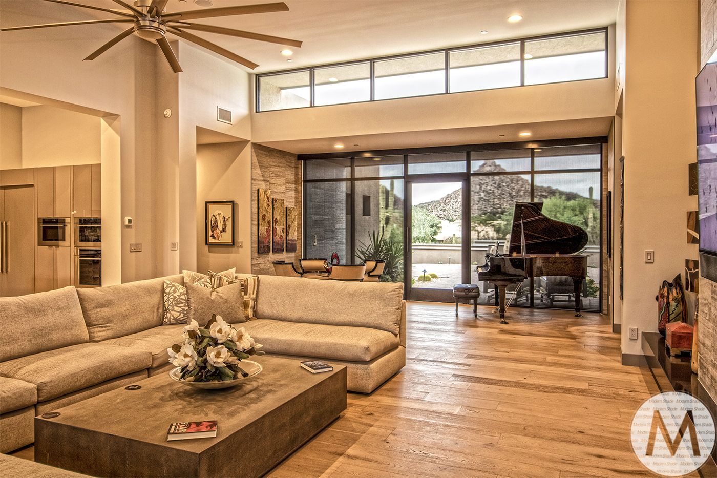 Modern living room with grand piano, large windows, and beige sectional sofa.