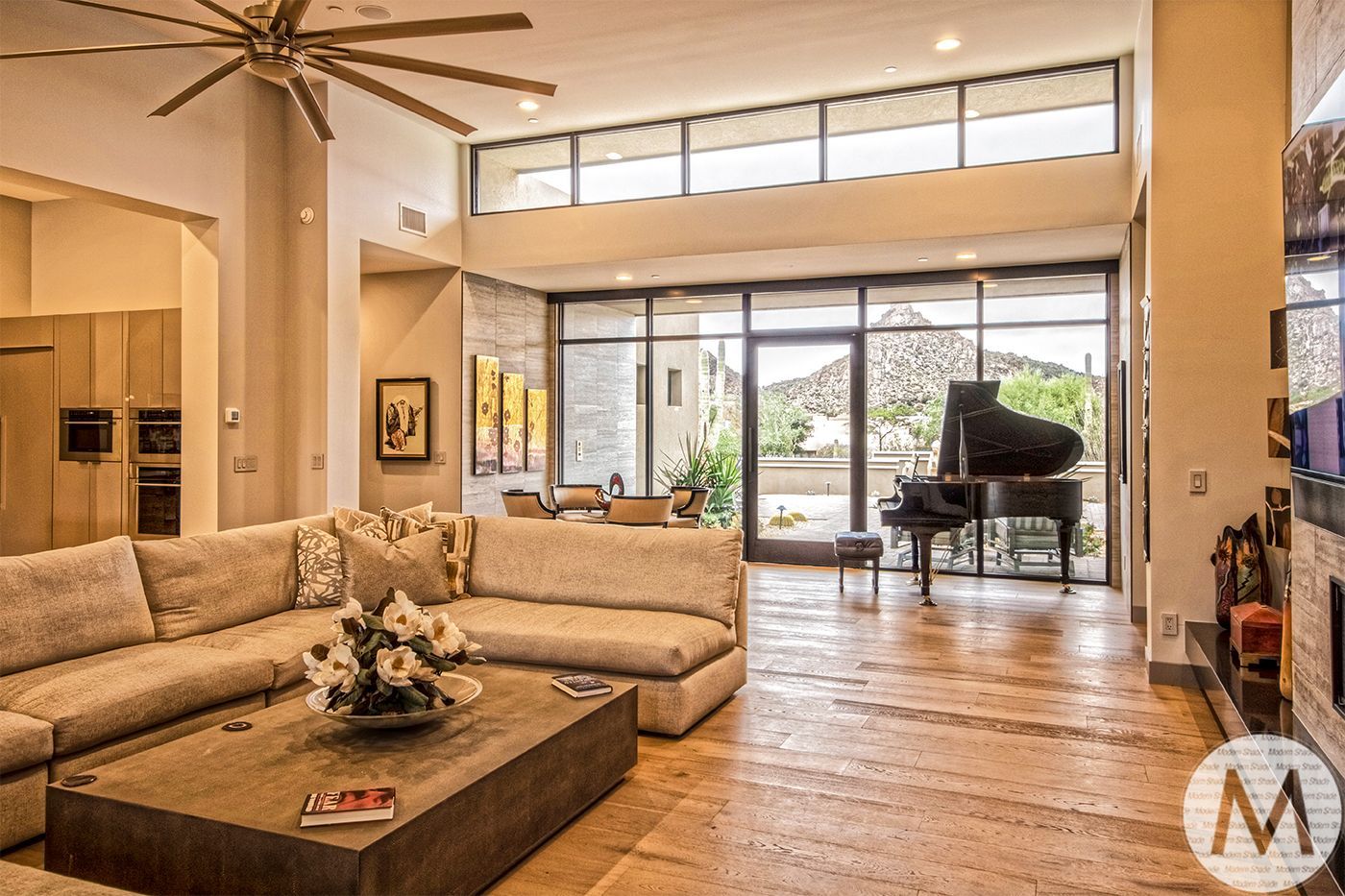Spacious living room with a grand piano, beige sectional sofa, and mountain view through large windows.