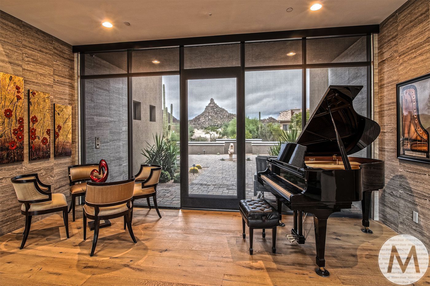 Grand piano in a room with patio doors, desert view. Armchairs, artwork, neutral colors.