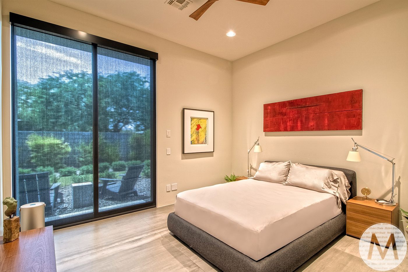 Bedroom with bed, artwork, large window with outdoor view, and a wooden nightstand.