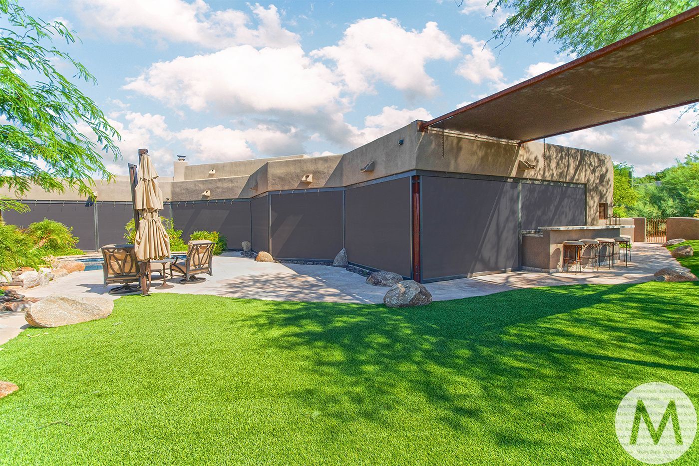 Backyard with green lawn, patio furniture, outdoor kitchen, and shade structure.