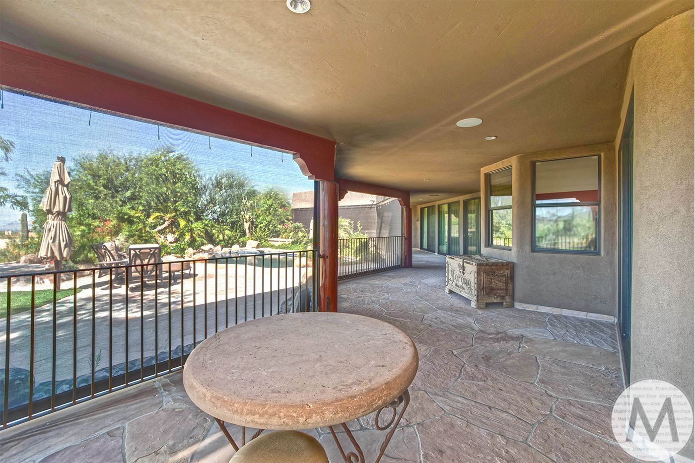 Covered patio overlooking a pool area with a stone table, shade screens, and desert landscaping.