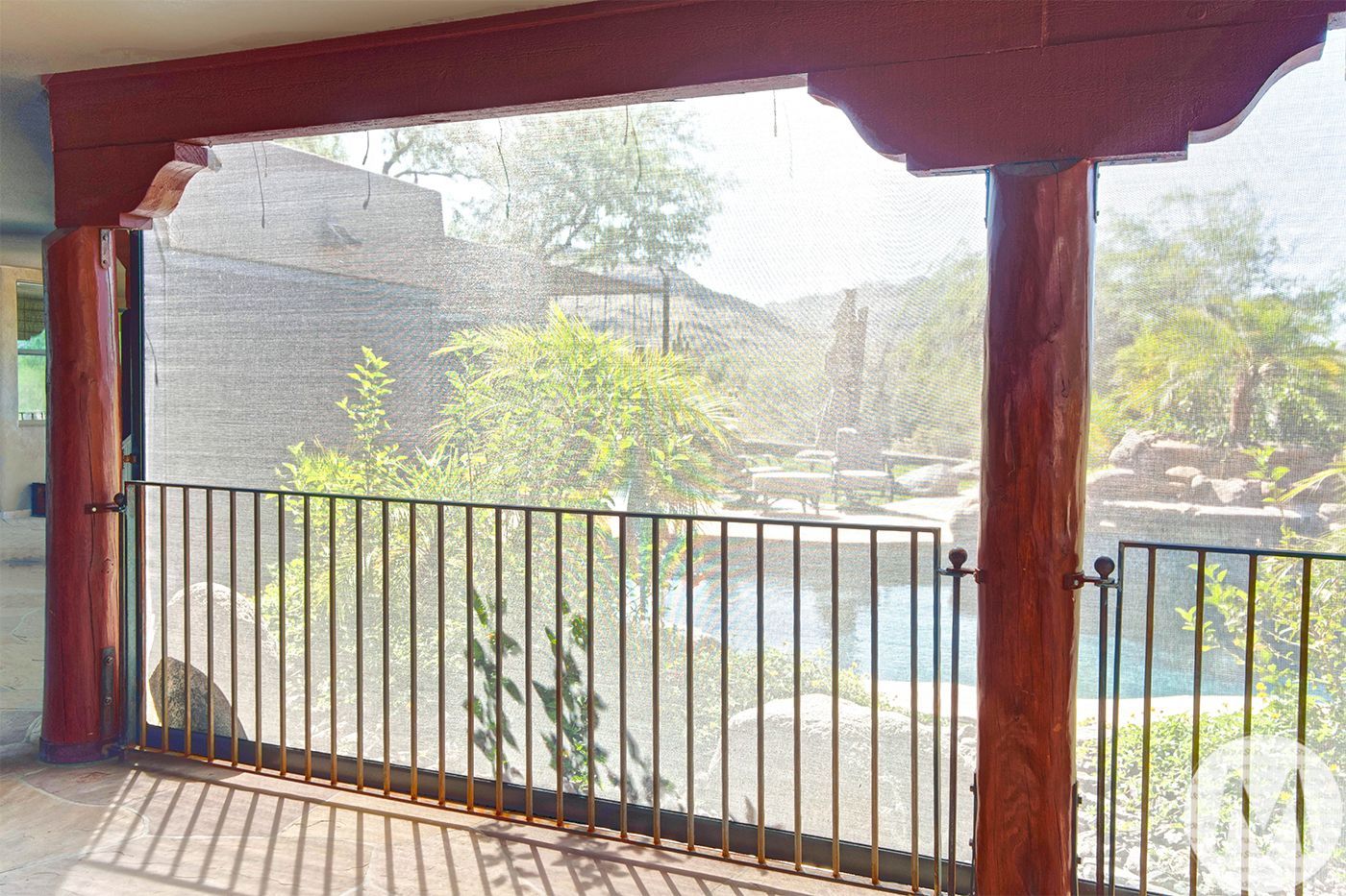 Covered patio with pool view, wood beams, iron railing, shade screen.