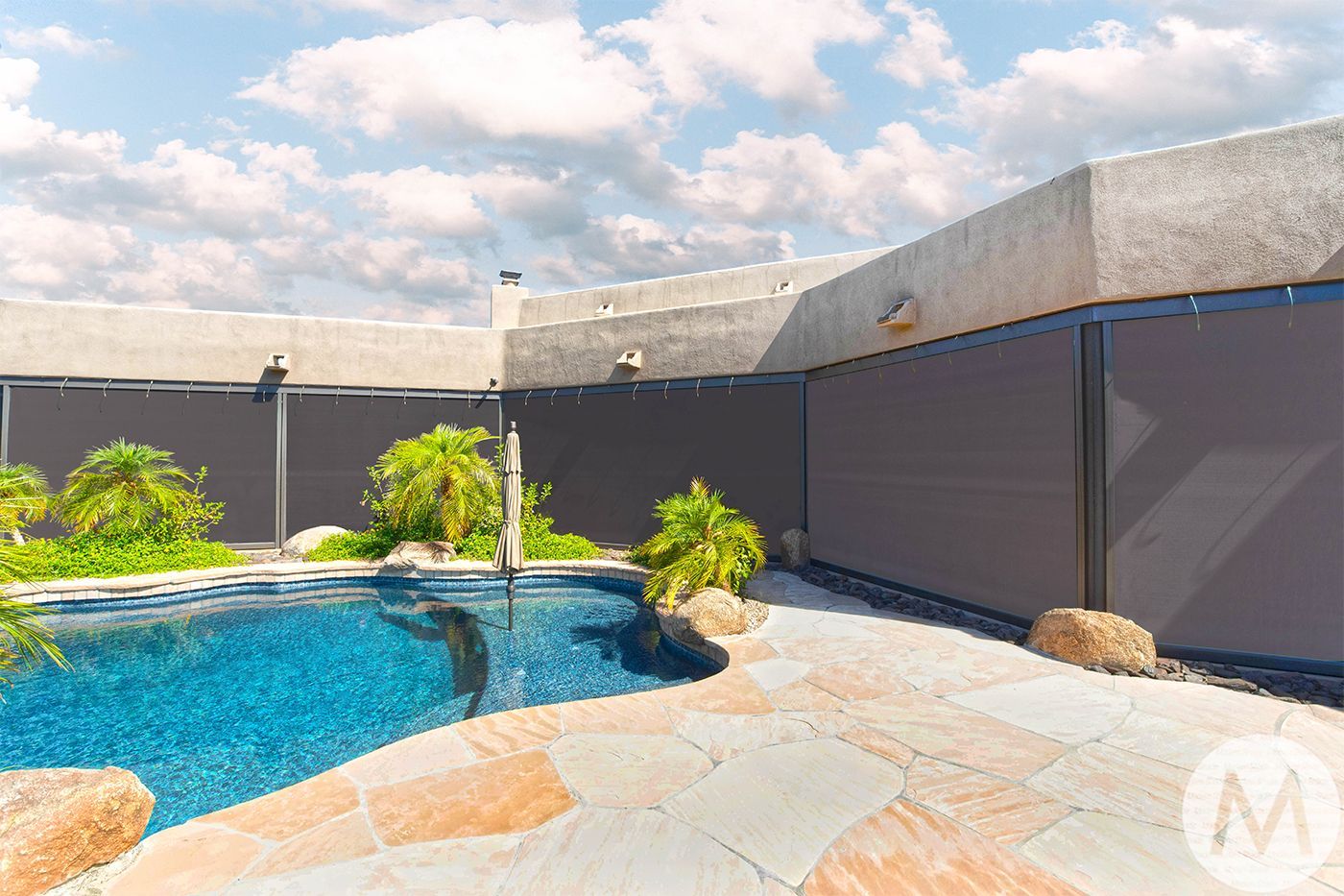 Poolside view with brown sun shades, blue water, stone patio, and cloudy sky.