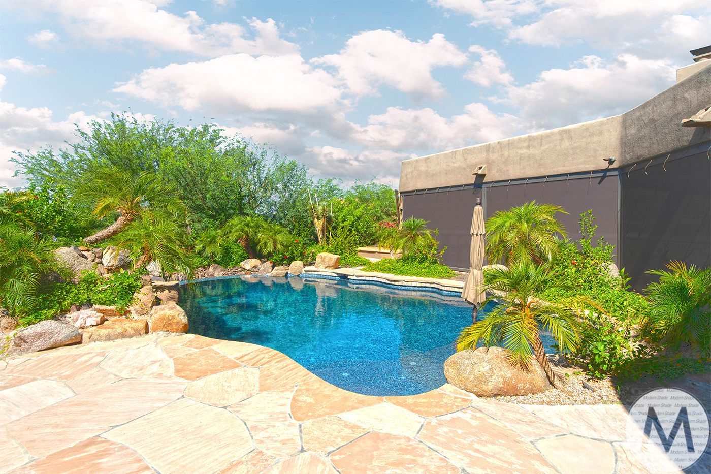 Swimming pool with blue water, surrounded by landscaping and stone patio under a blue sky.