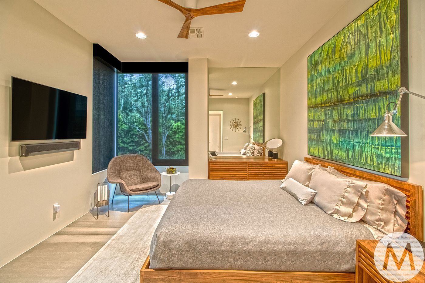Modern bedroom with a large window, TV, artwork, bed, and chair.