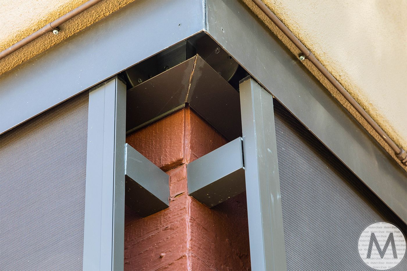 Corner of a window screen frame with gray metal and mesh, set against a brick exterior.