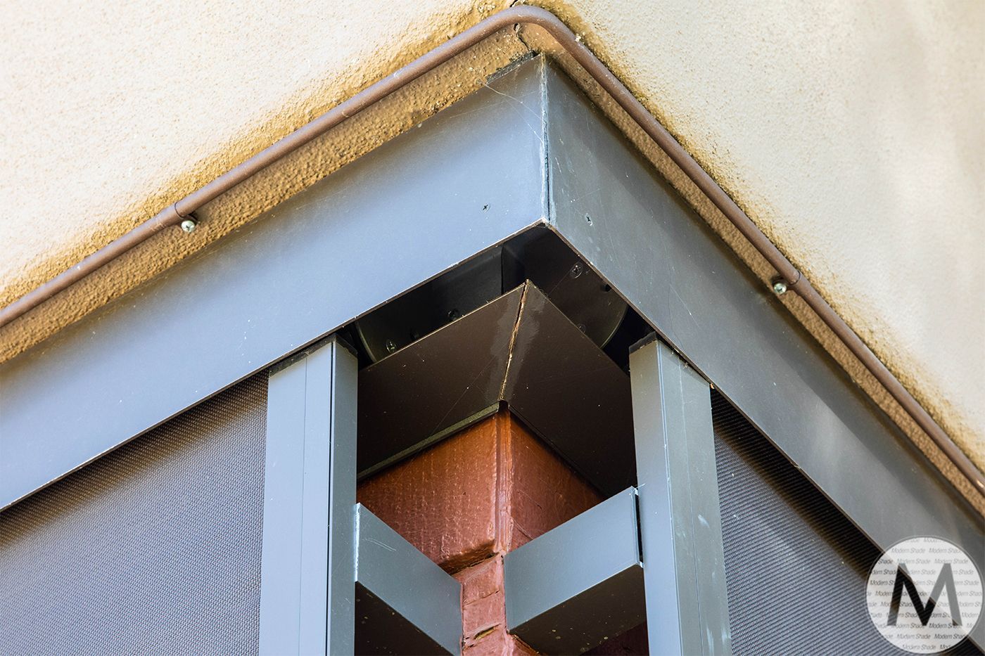 Close-up of a corner of a screened window with gray painted trim and a brick corner.