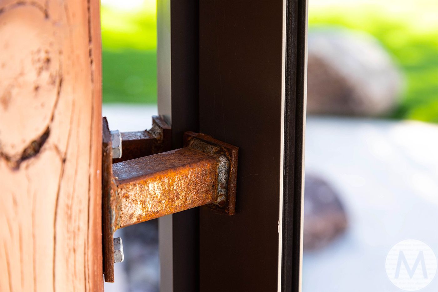 Close-up of a weathered, rusty metal hinge connecting a wooden door to a brown door frame.
