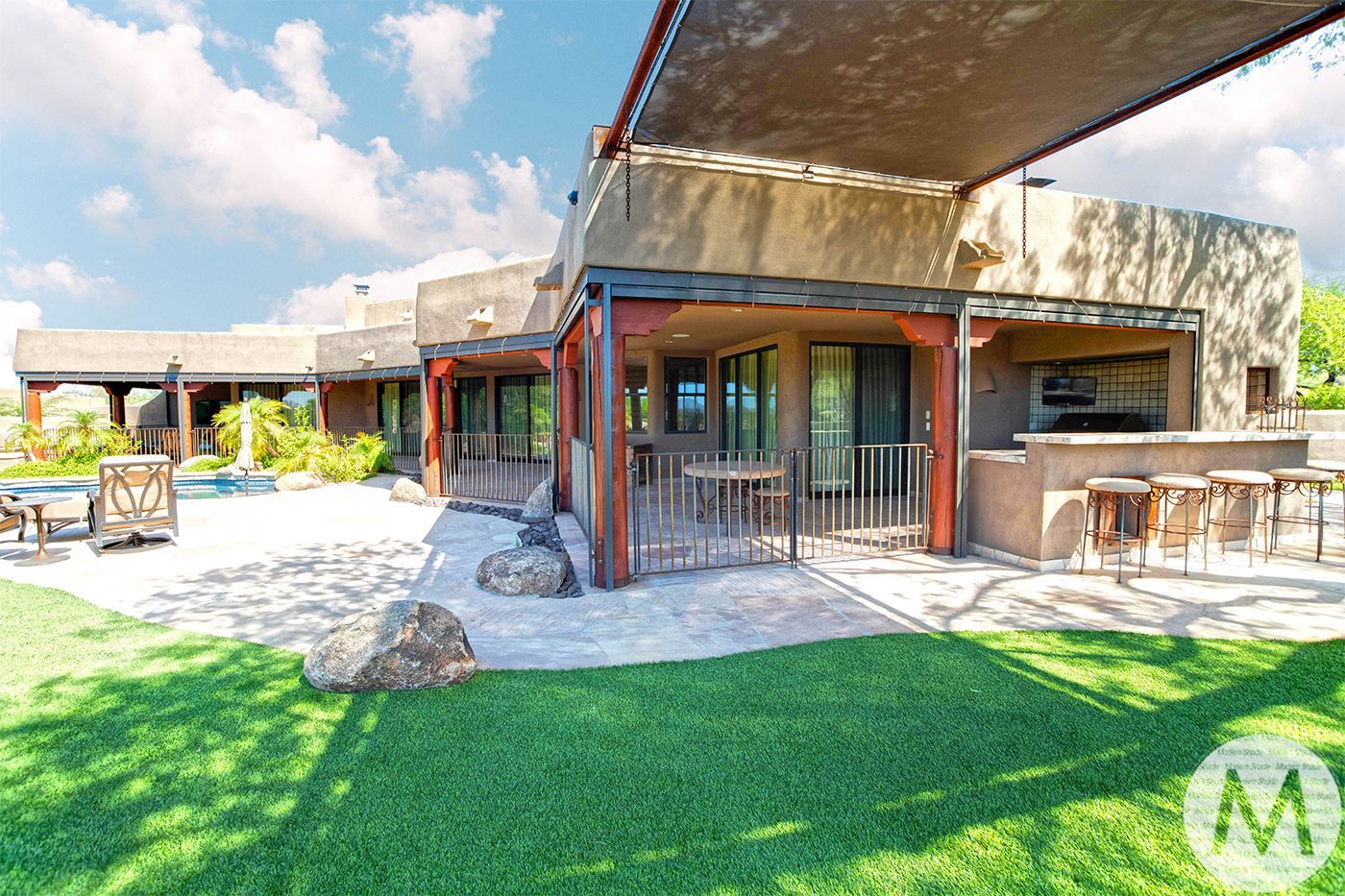 Patio of a desert home with lawn, outdoor kitchen, and swimming pool.