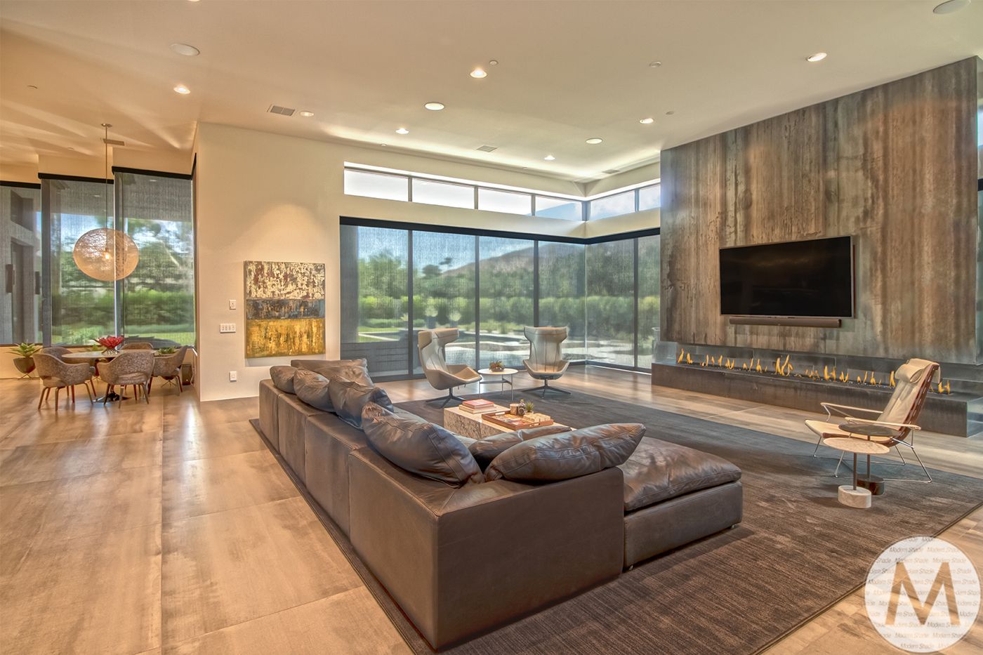 Modern living room with gray sectional, fireplace, and large windows overlooking a yard.