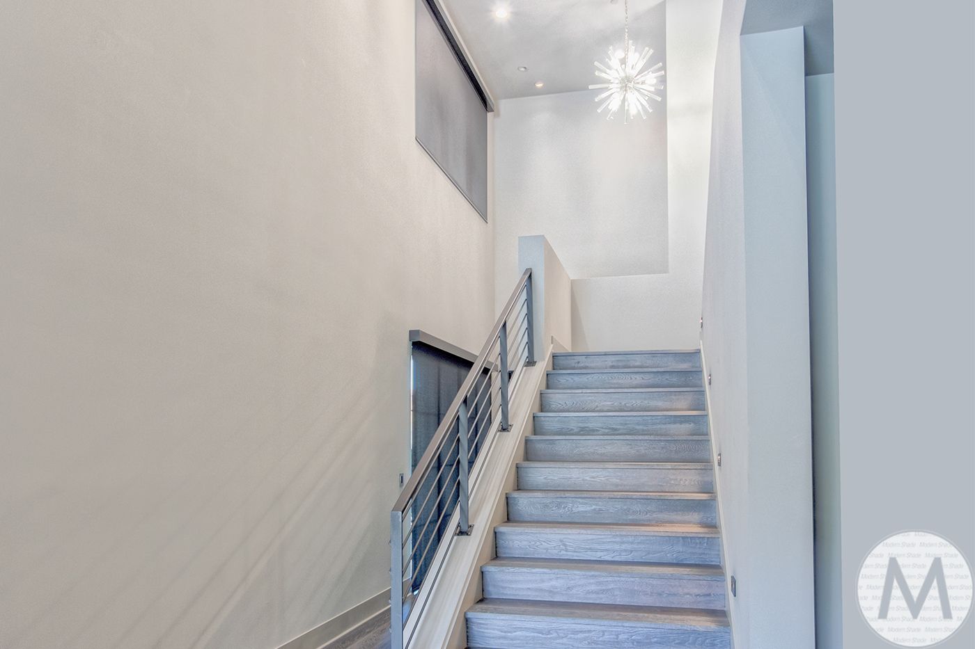 Staircase with gray steps, white walls, metal railing, and a hanging light fixture.