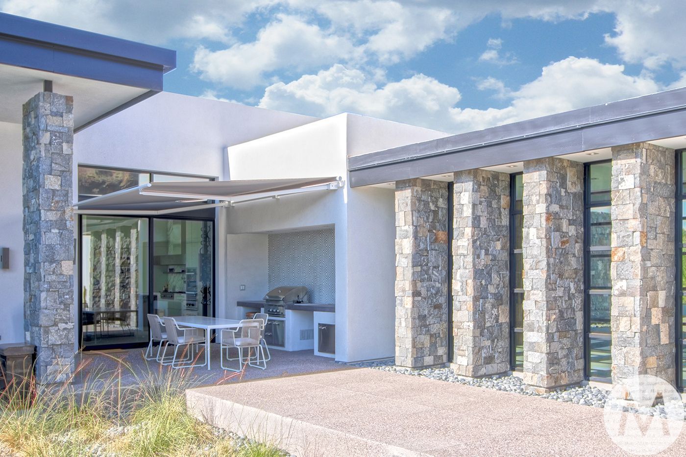 Modern home exterior with stone columns, outdoor kitchen, and patio furniture.