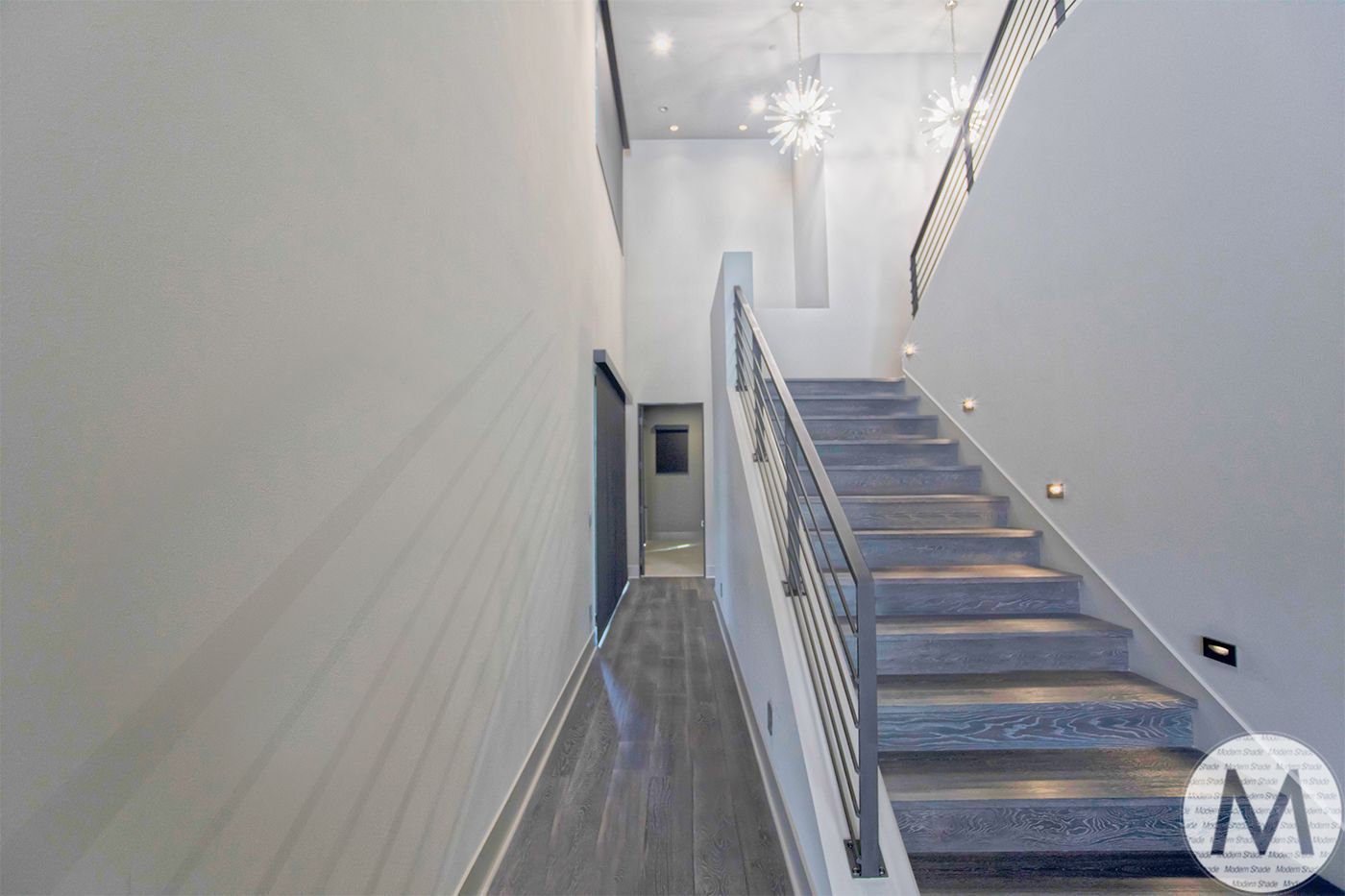 Modern staircase with gray carpet, metal railing, and lights.