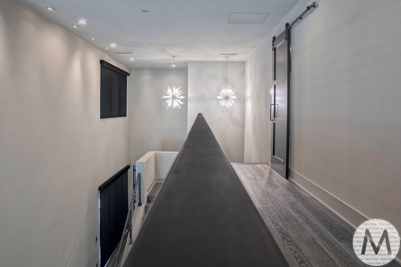 Narrow hallway with a dark metal handrail, a dark barn door, and decorative wall lights.