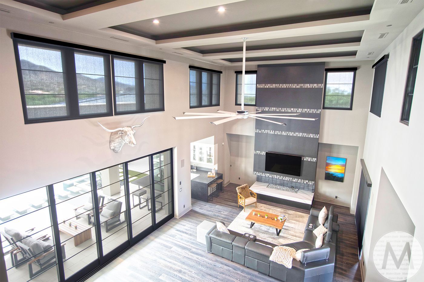 High-ceiling living room with large windows, fireplace, and modern furniture.