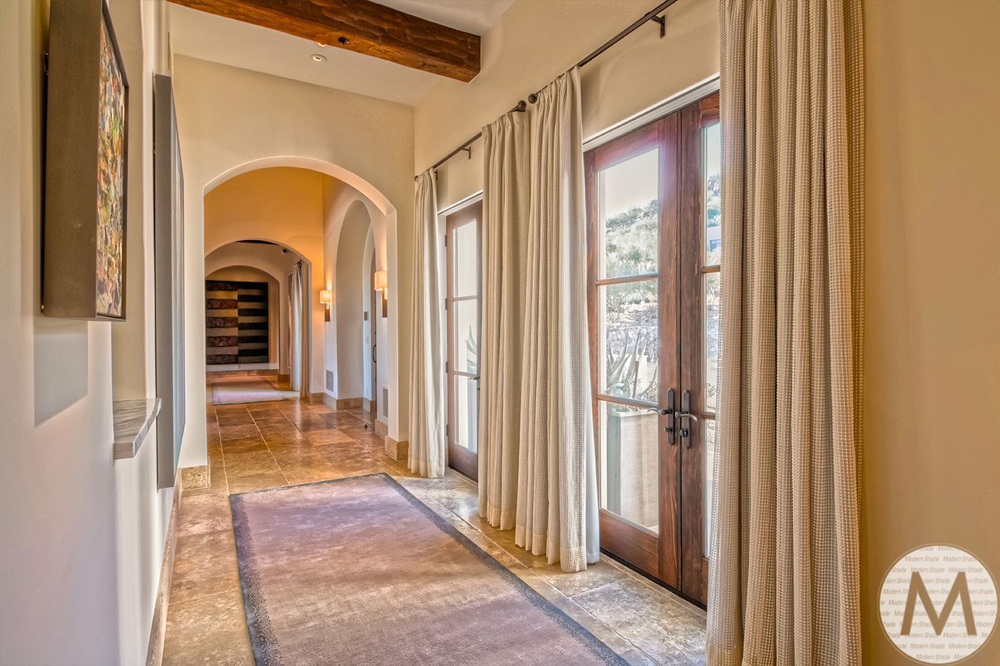 Hallway with arched doorways, wooden doors, and marble flooring.