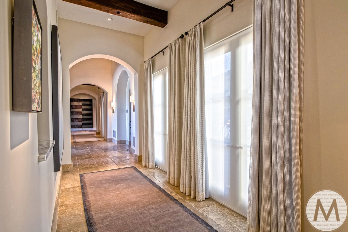 Hallway with arched doorways, stone floor, and sunlight streaming through sheer curtains.