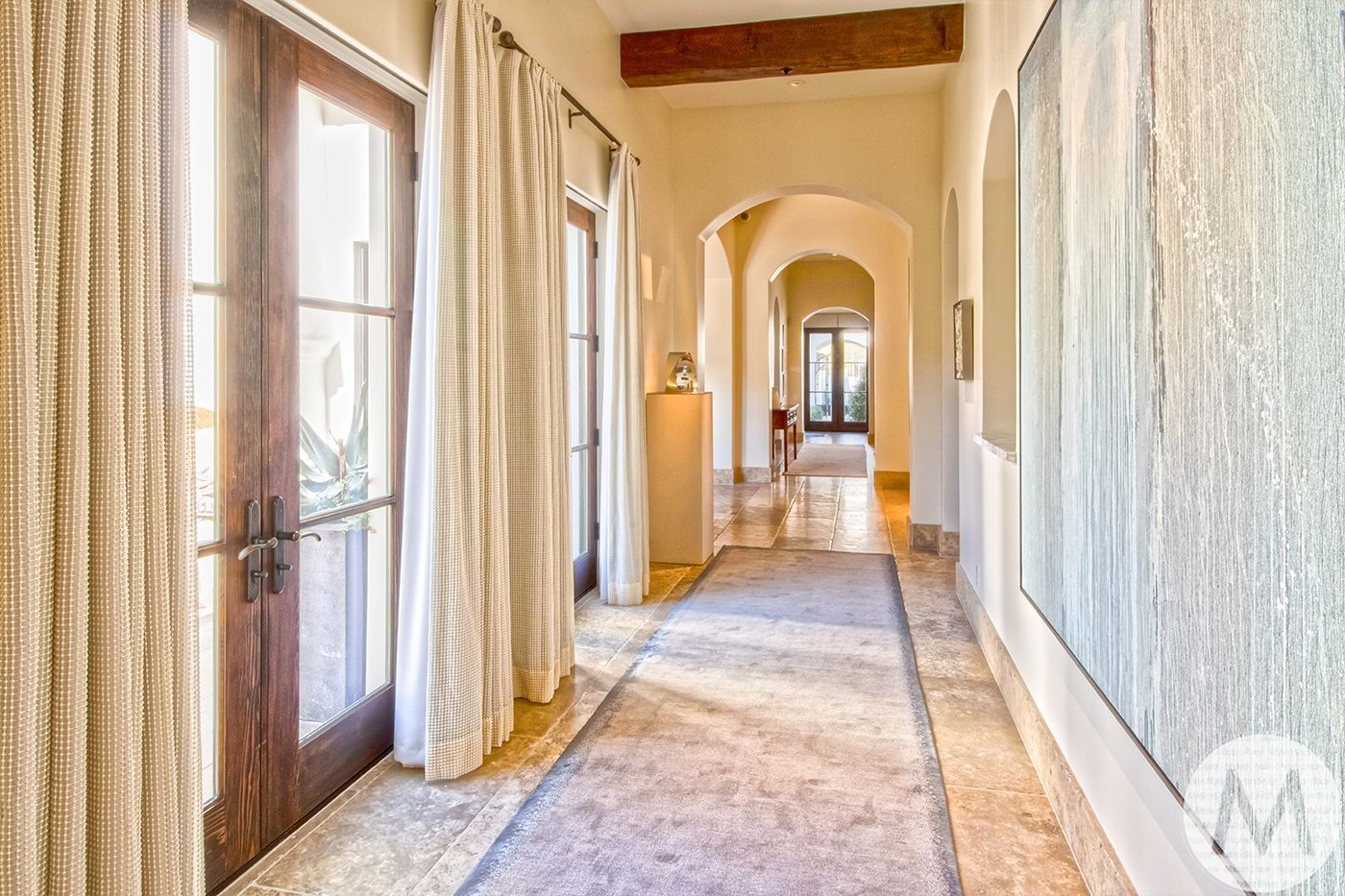 Hallway with archways, light walls, wood doors, cream curtains, rug, and artwork.