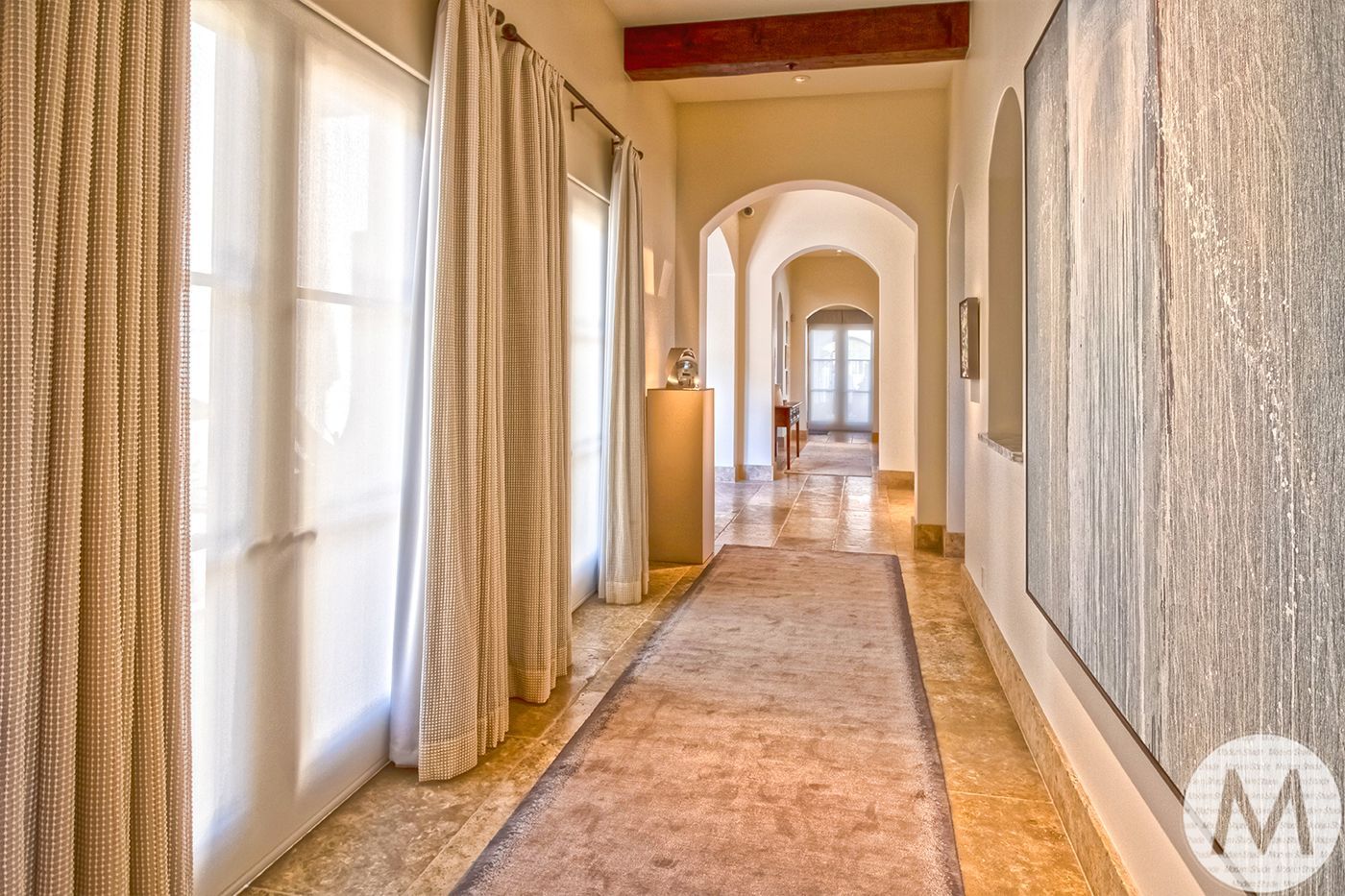 Long hallway with beige rug, arched doorways, and a large abstract painting.