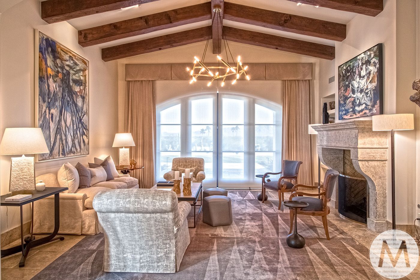 Living room with exposed beams, arched window, fireplace, beige and blue tones.
