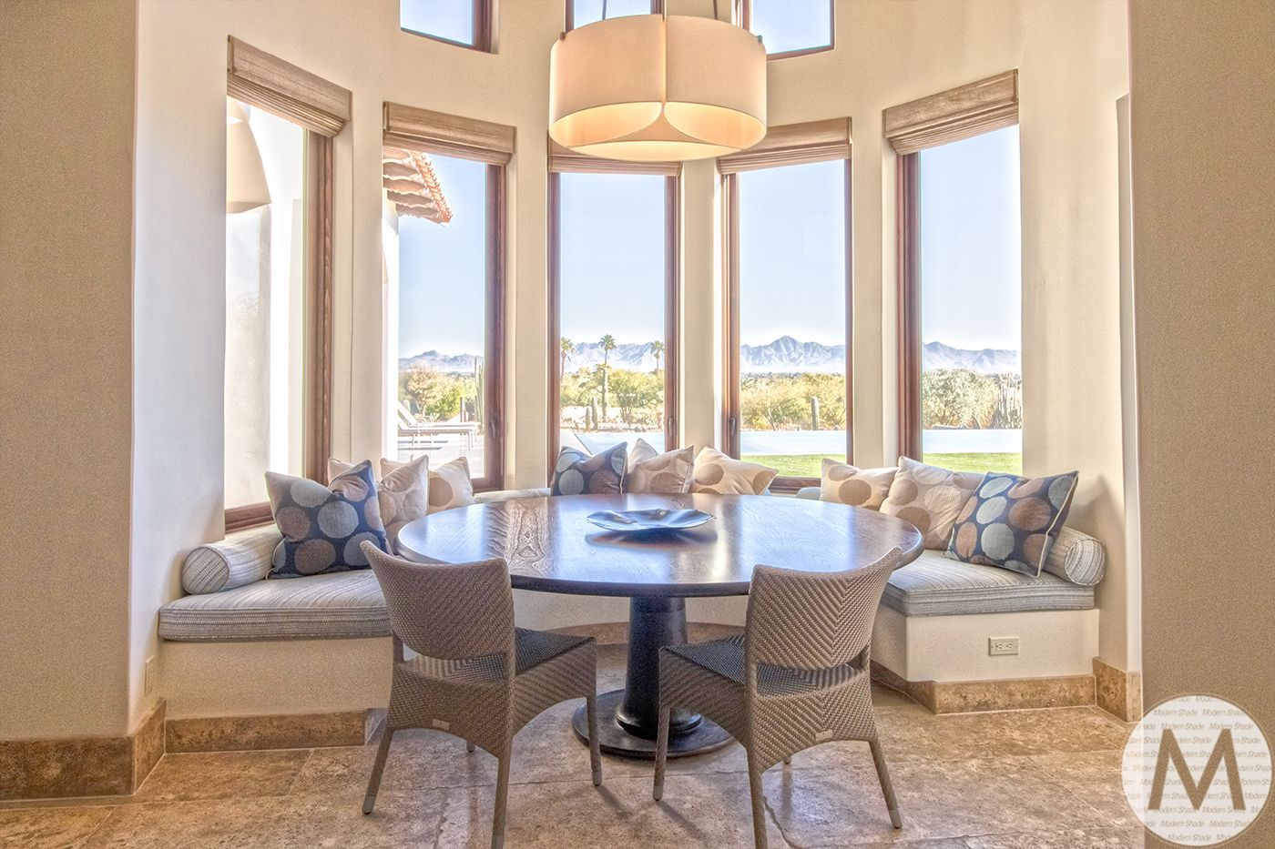 Dining area with round table, wicker chairs, built-in window seat, and large windows with a scenic view.