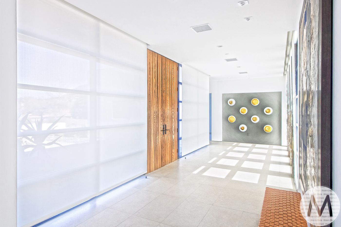 Hallway with white walls, wooden door, art, and bright natural light.