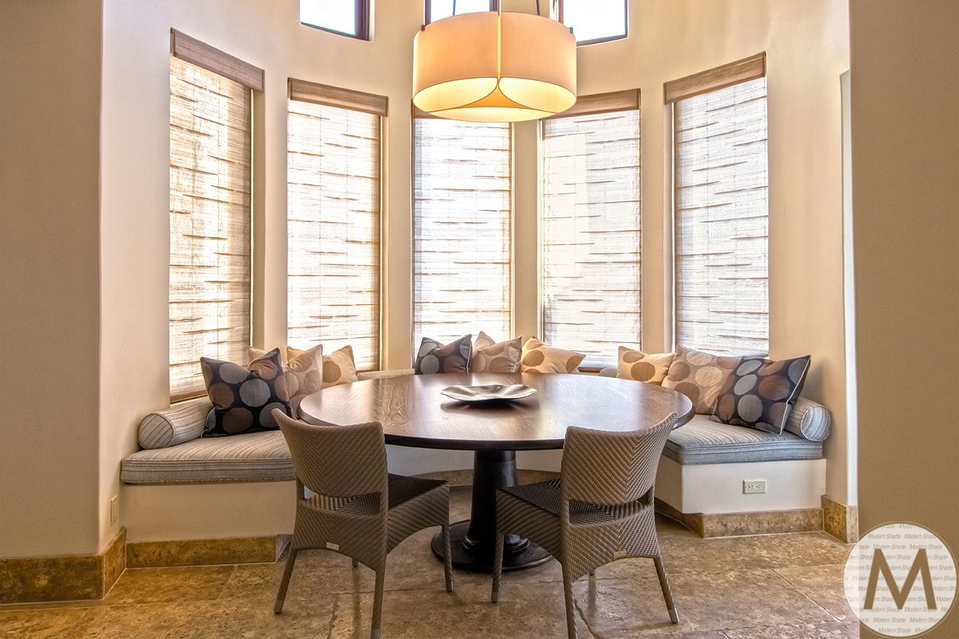 Circular dining area with a table, built-in bench seating, wicker chairs, and a large window.