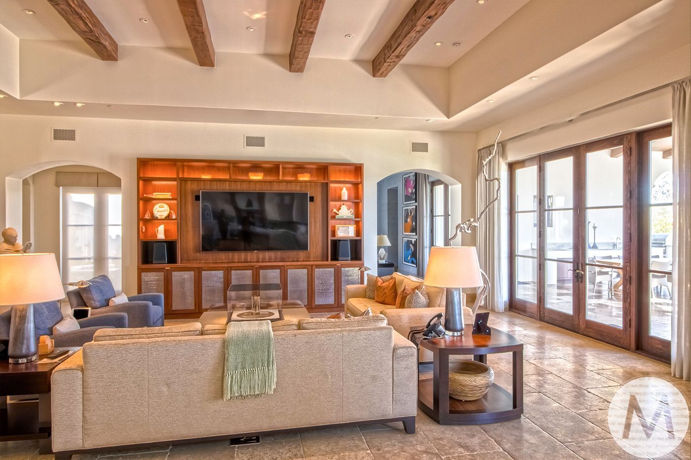 Spacious living room with large TV, built-in shelving, wood ceiling beams, and French doors.