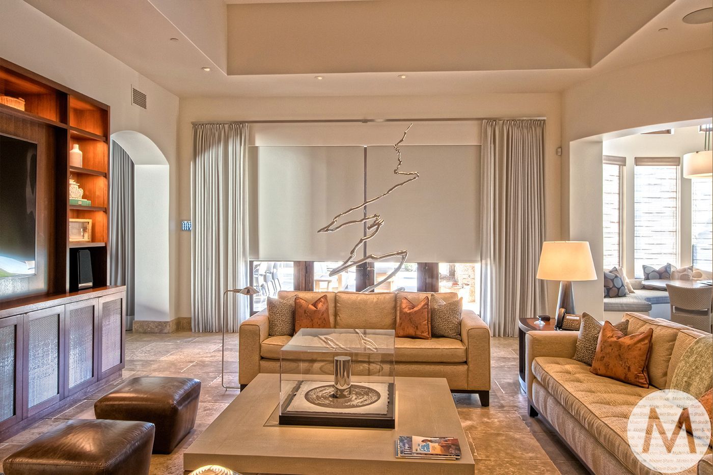 Luxurious living room with beige couches, large TV, and decorative branches in a sunny setting.