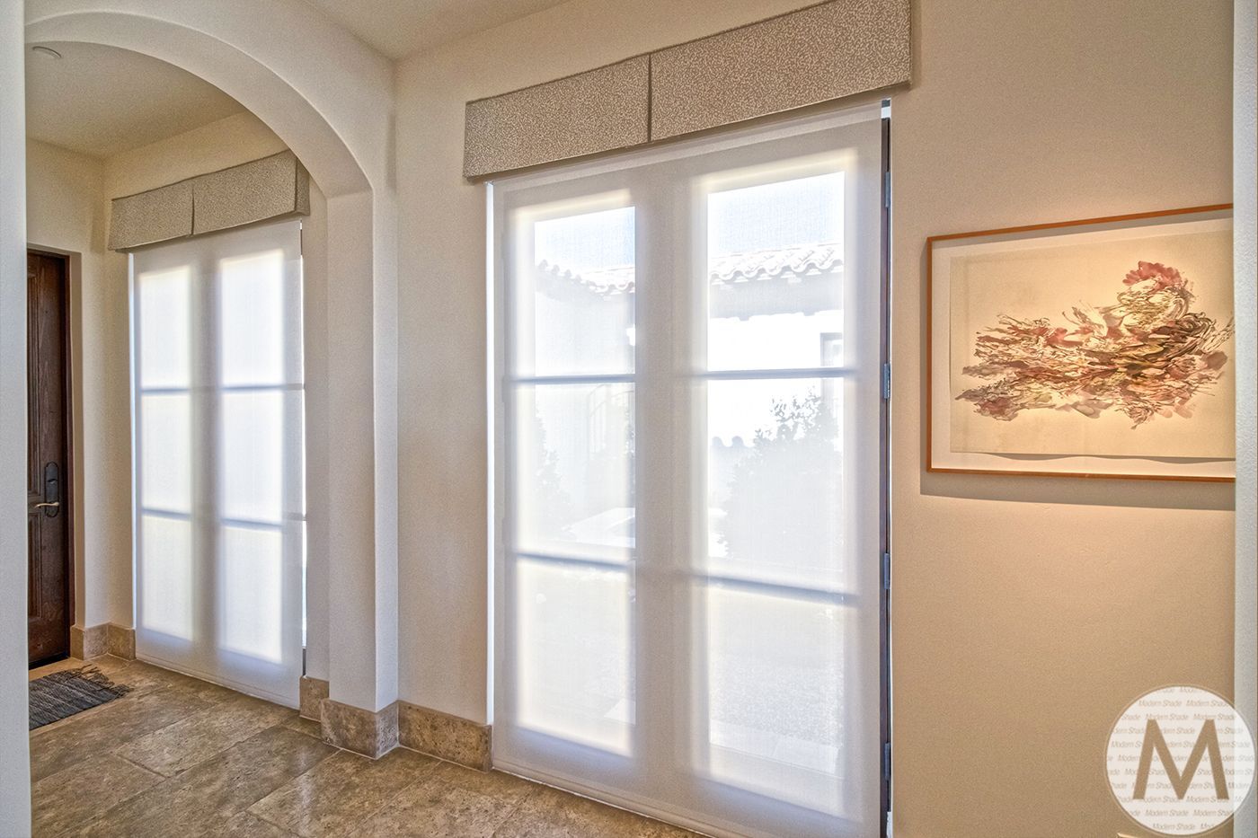 Hallway with arched doorway and windows, cream walls, light filtering shades, and artwork.