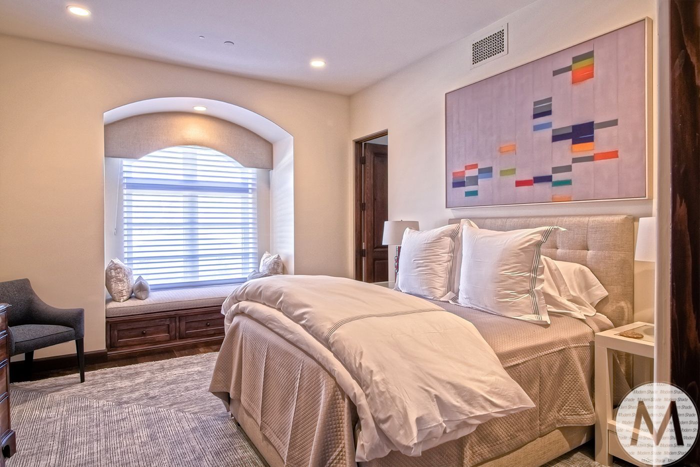 Bedroom with a bed, window seat, chair, and colorful abstract artwork.